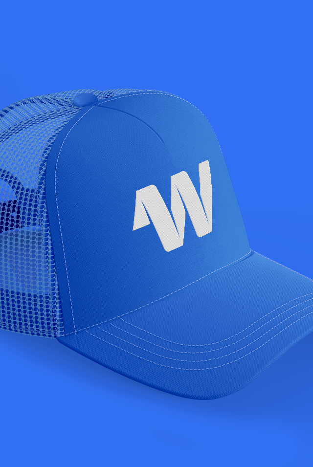 A royal blue trucker hat with a white logo consisting of a stylized "W" on the front panel. The hat features a mesh back with a white stitching detail, giving it a casual and sporty look. The hat is seen against a matching blue background, blending into the scene except for the contrast of the white logo.